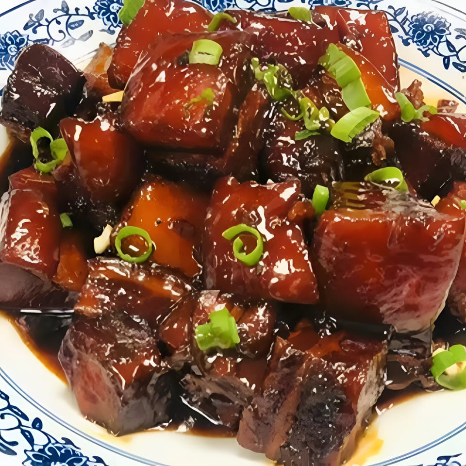 Braised pork belly, glistening with dark sauce and garnished with green onions, on a white and blue plate.